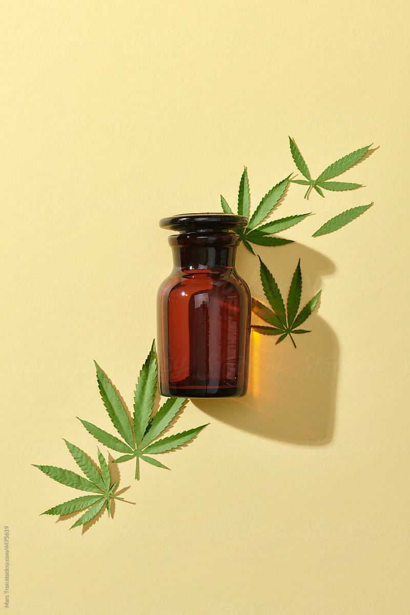 Glass brown bottle with cannabis oil and hemp leaves