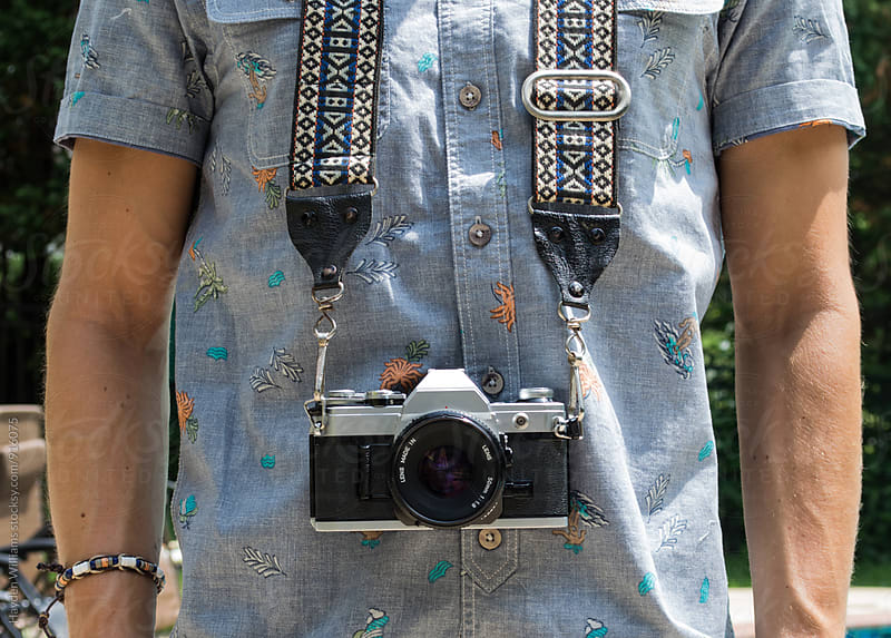 Man with vintage film camera and camera strap around neck on bright summer day