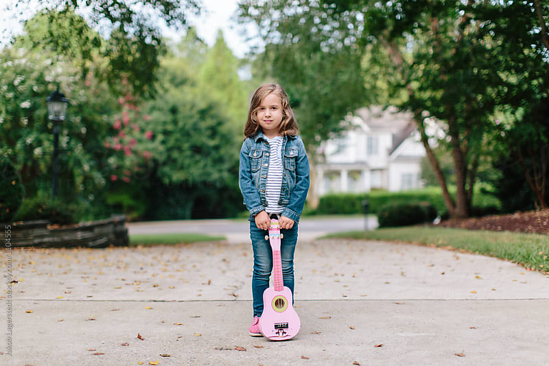 Cute young girl standing with a toy guitar leaning against her
