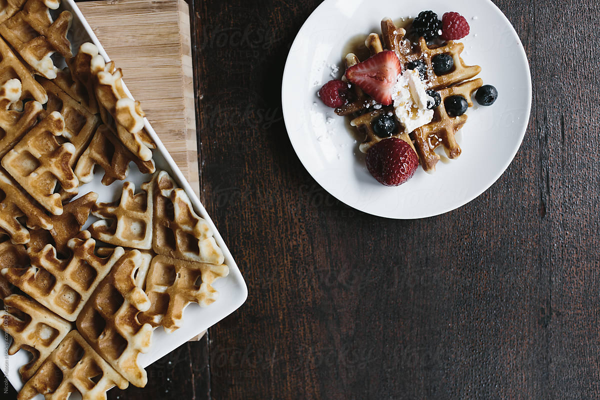 tray of waffles beside plate of waffle and berries