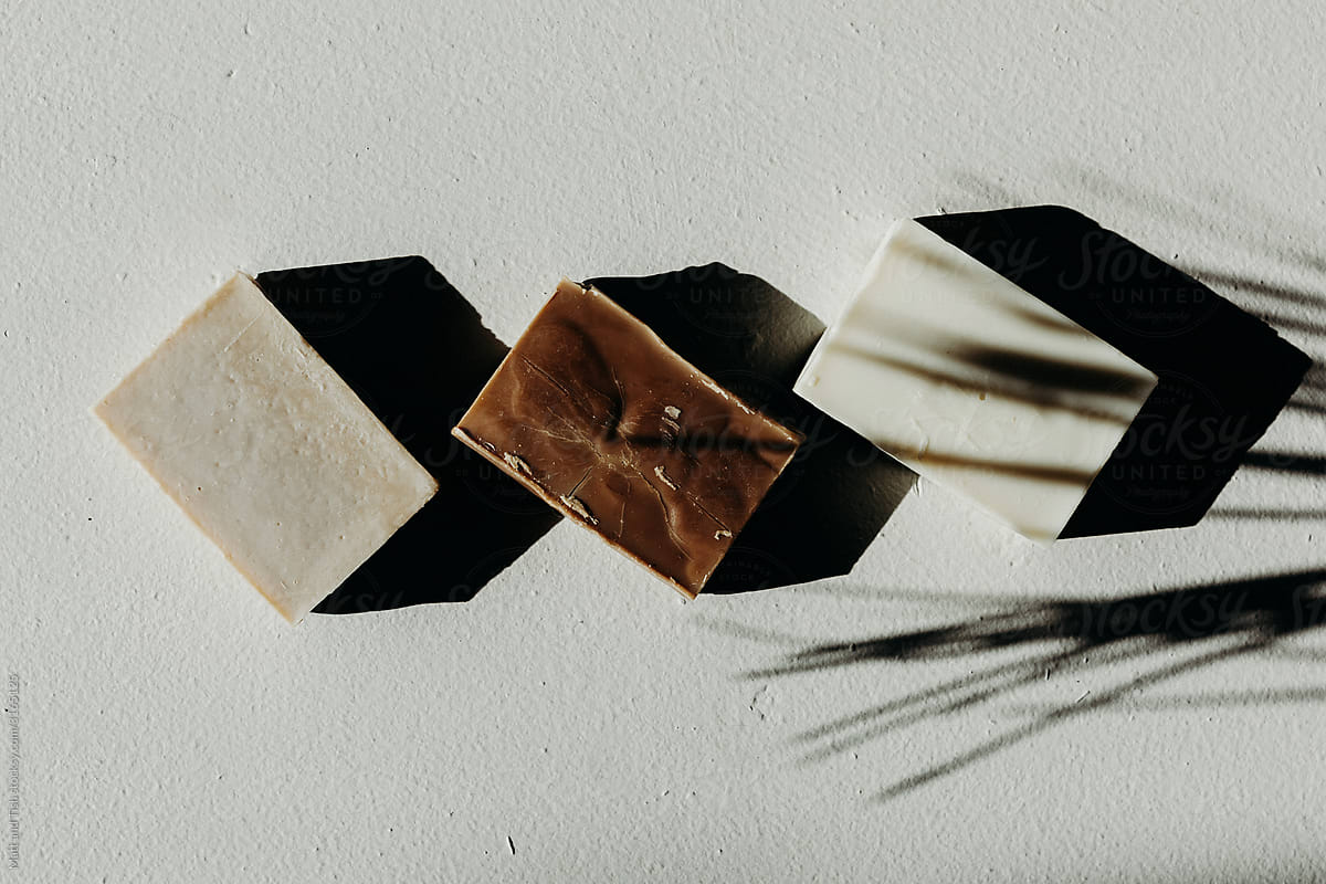 Minimal Still Life of Three Rectangle Bars of Soap in a Palm Leaf Shadow on White Cement. Three different colors of soap.