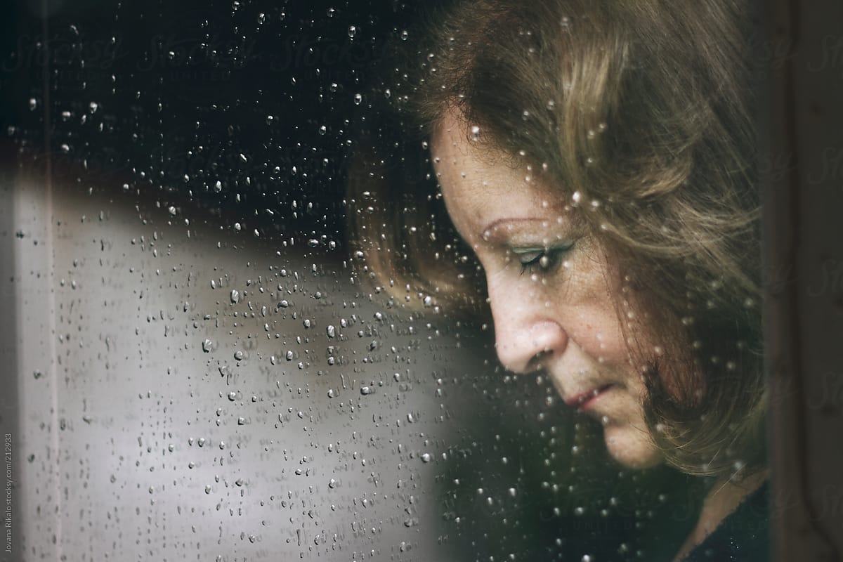 Mature woman standing at the window watching the rain