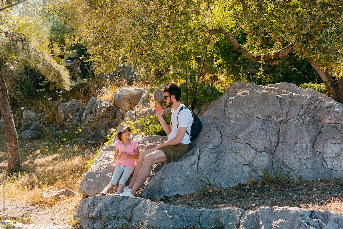 Kid and young man resting on a rock in a green area