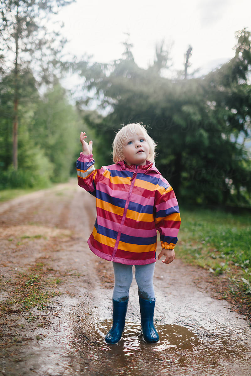 Little kid dressed in multicolor raincoat on the forest path