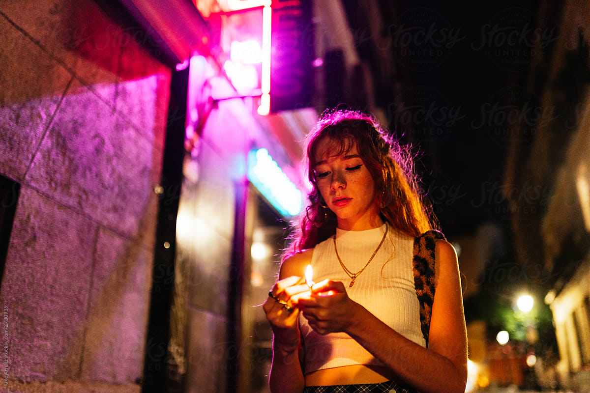 attractive ginger woman lighting a match on street at night