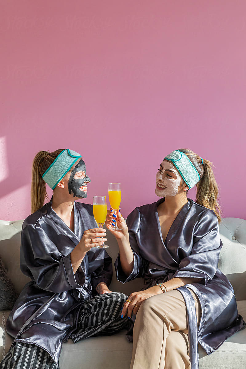two women with beauty masks smiling and drinking a mimosa