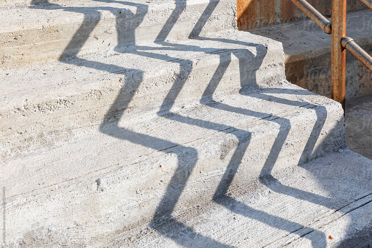 Close-up of rough concrete stairs and railing shadows.