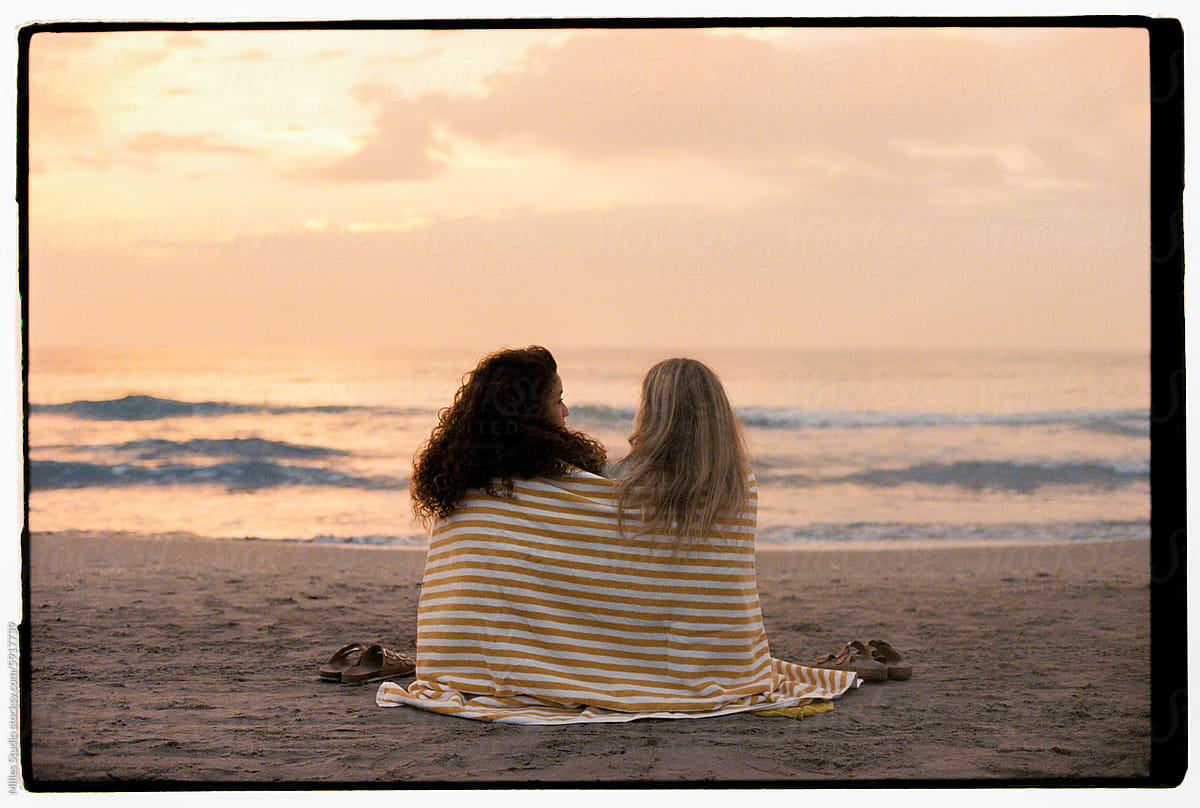 Female friends sitting on sandy beach and admiring sea