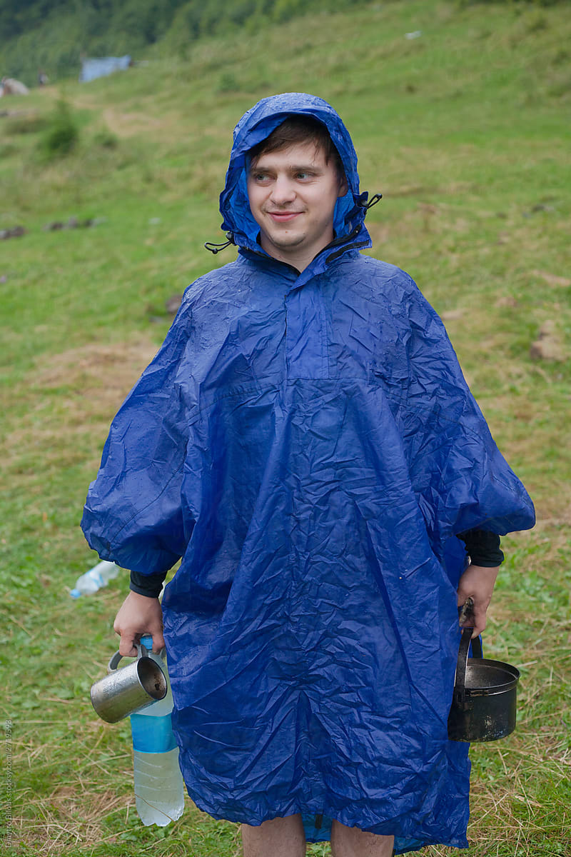 the guy in the blue raincoat holds water, a mug and a bowler in his hands and smiles
