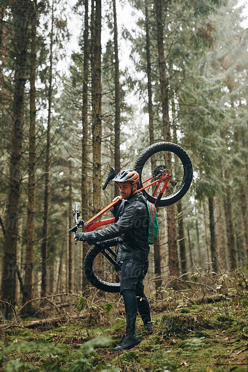 Lone rider carrying his mountain bike in a misty forest
