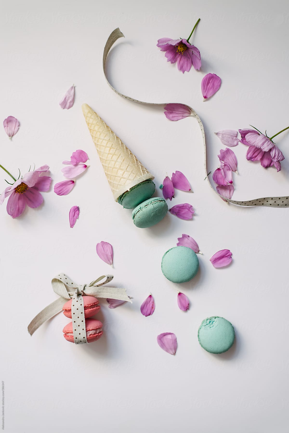 Turquoise and pink macaroons in cone with pink flowers on white background