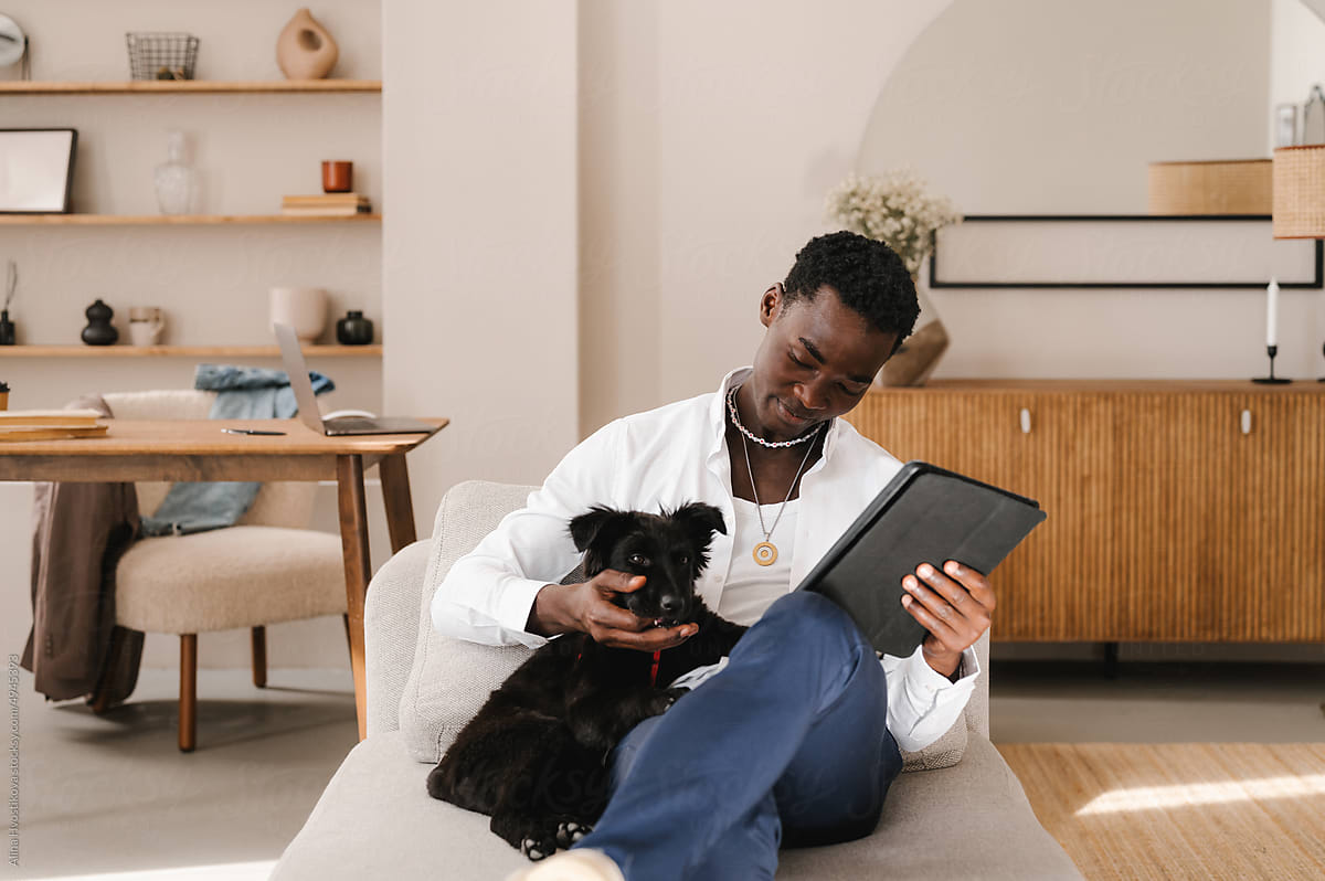 Young  guy caressing dog and using tablet at home