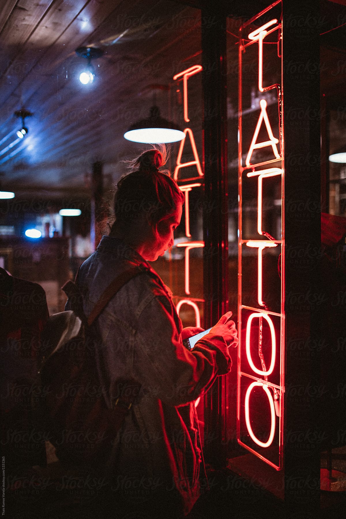 woman looking her phone at night in front of a tattoo shop