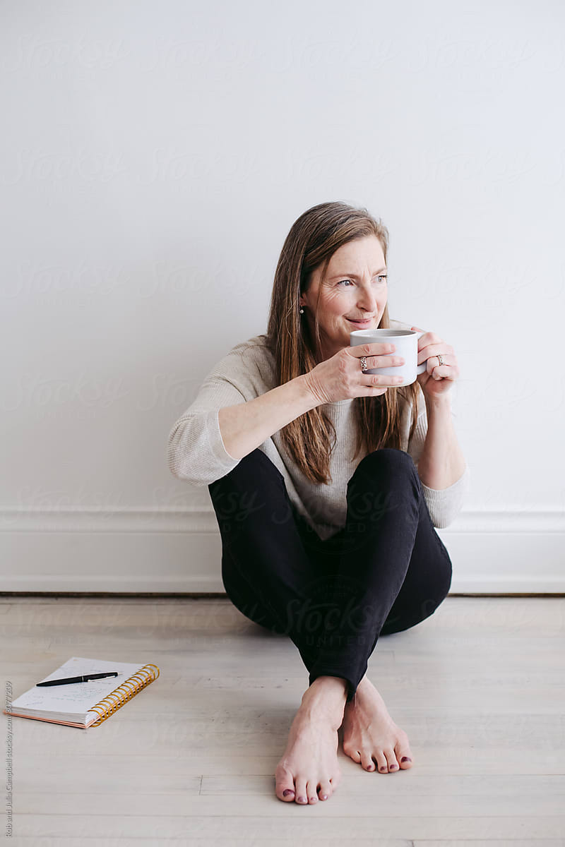 Mature woman sitting on floor enjoying tea or coffee and journaling