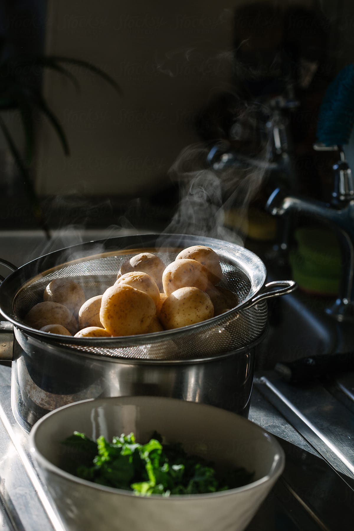 Freshly cooked new potato\'s with steam coming from them,draining by the kitchen sink.