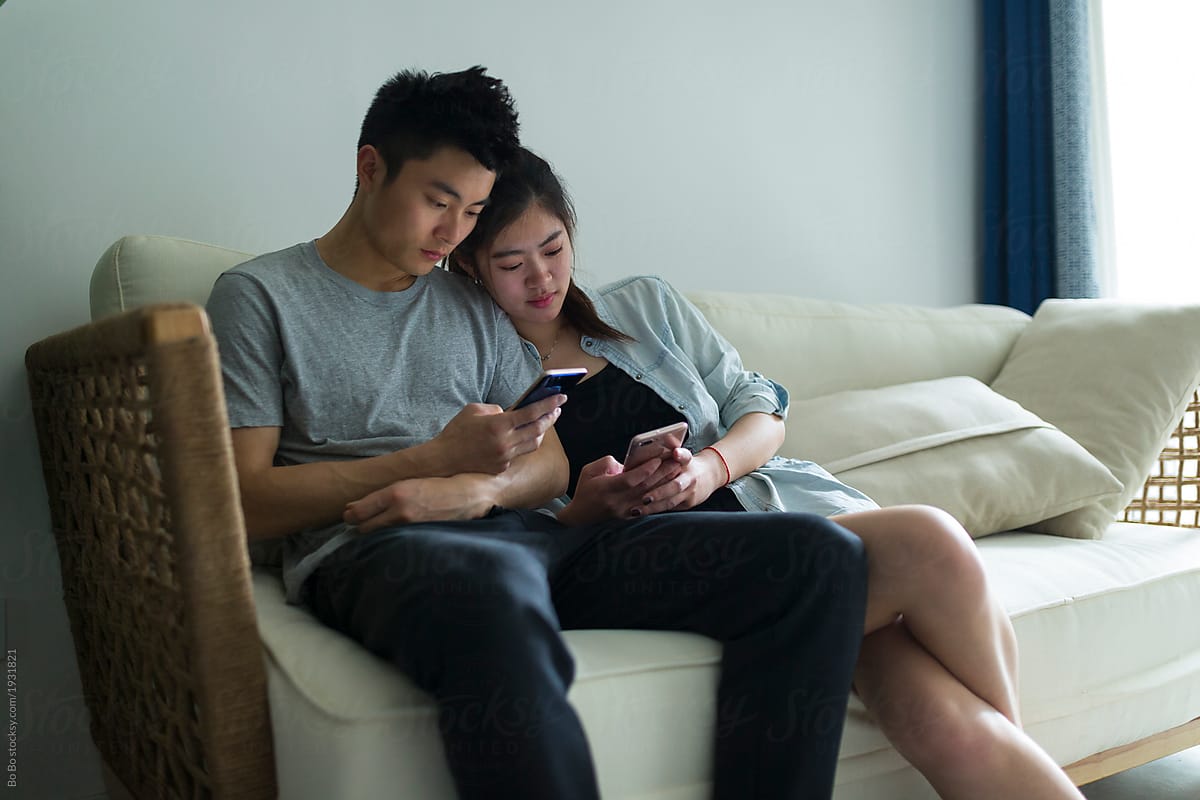 Young asian couple looking at mobile phone in home