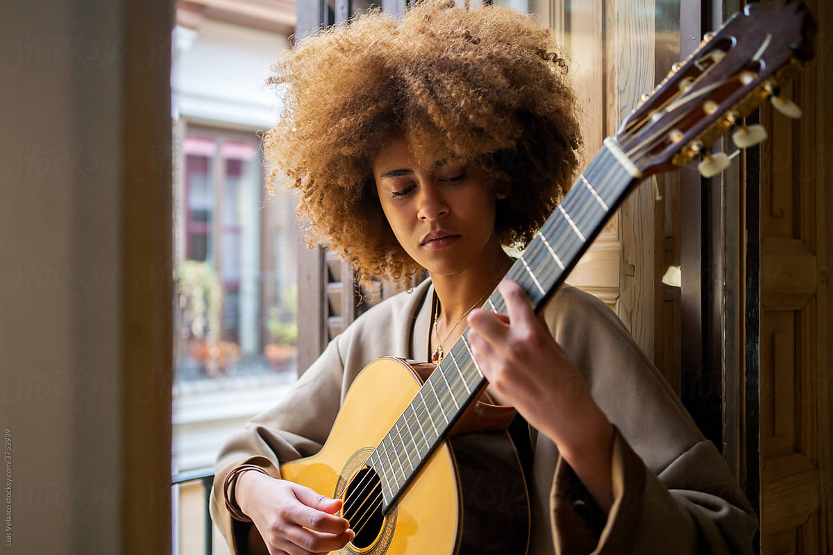 Black Woman Playing Music With The Guitar Next To The Window.