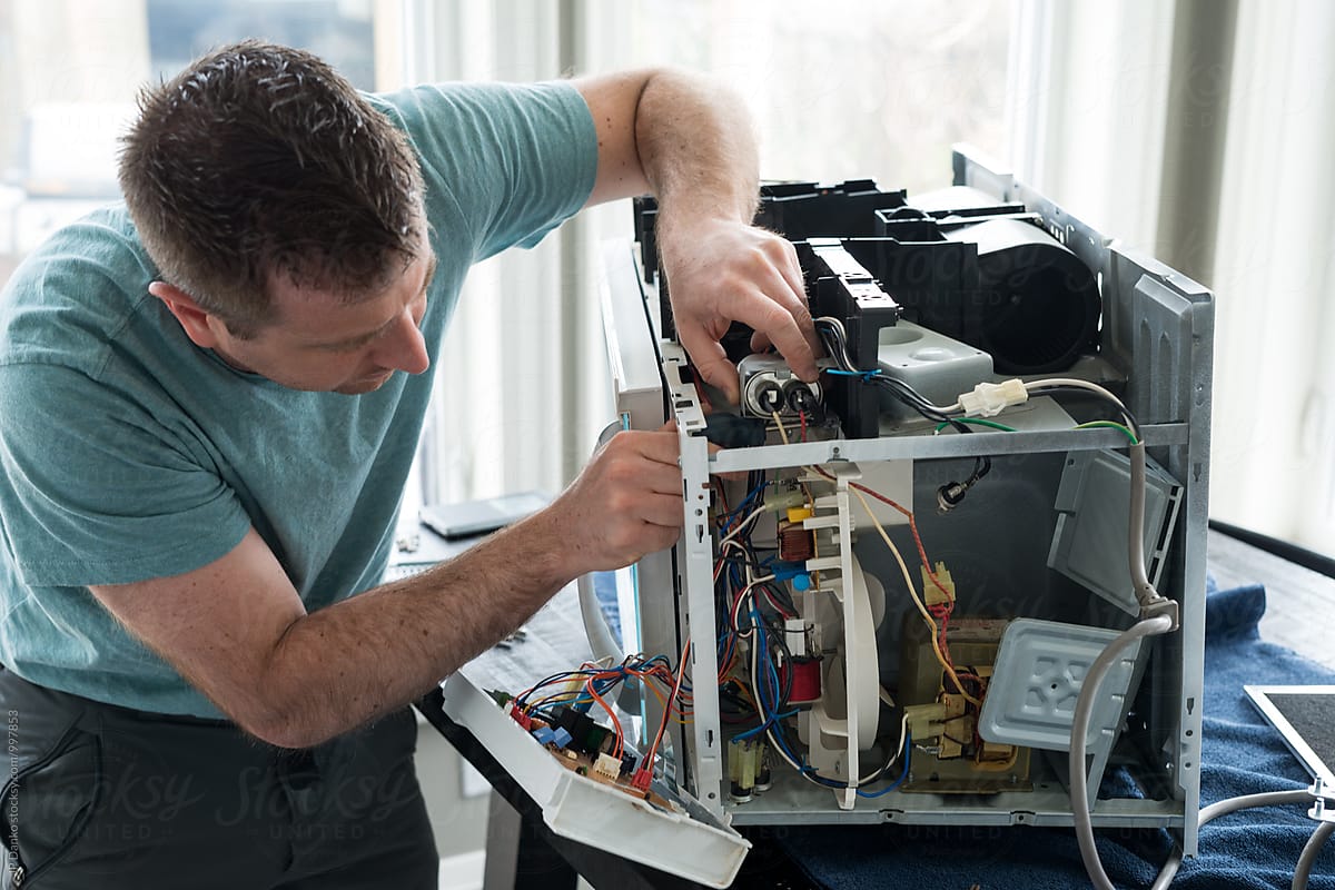 Man Fixing Broken Microwave Oven Appliance In Kitchen
