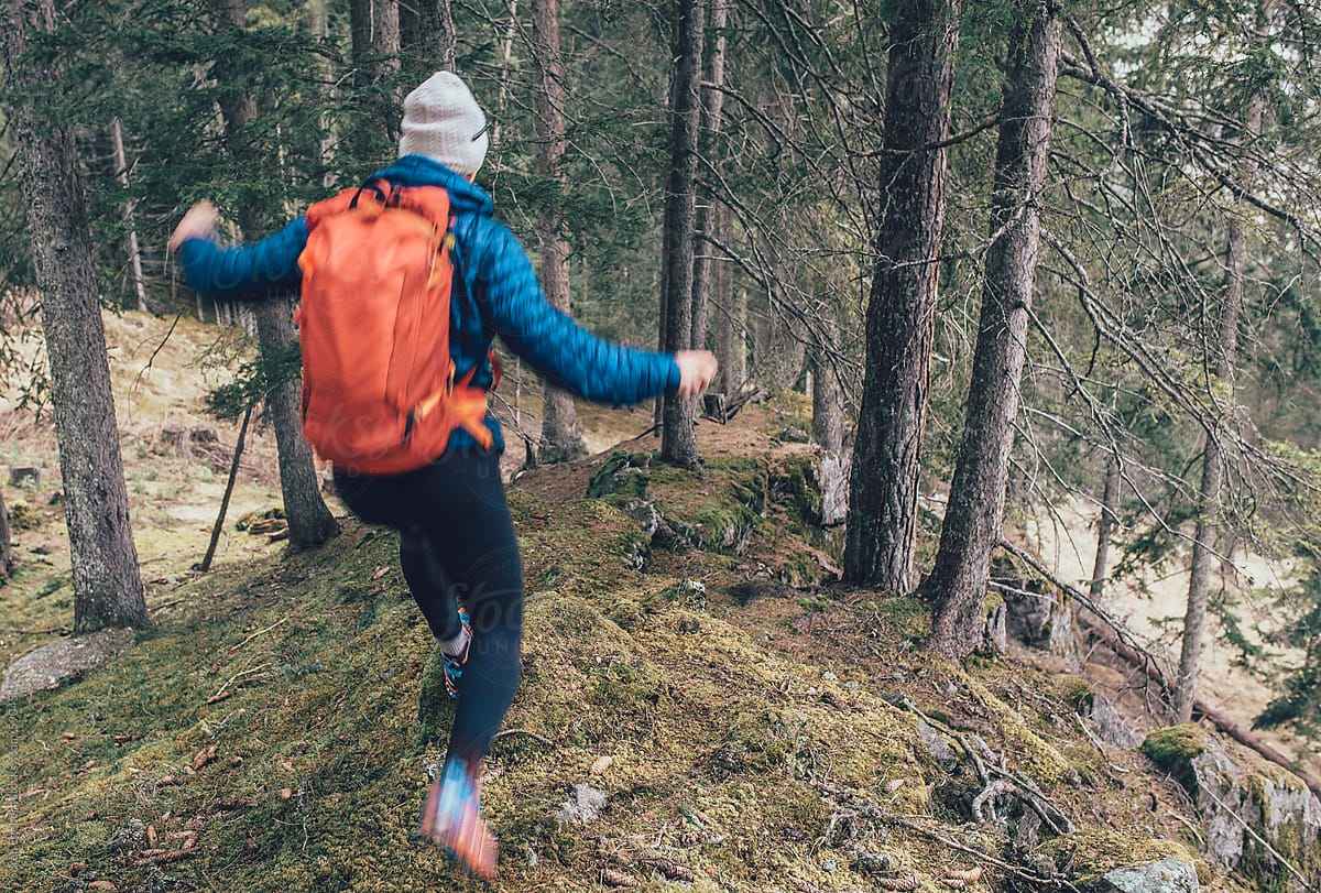 Hiker with backpack jumping downhill through a mountain forest