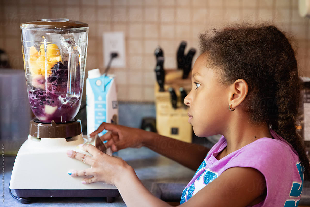 Young girl using a blender to make a fruit smoothie.