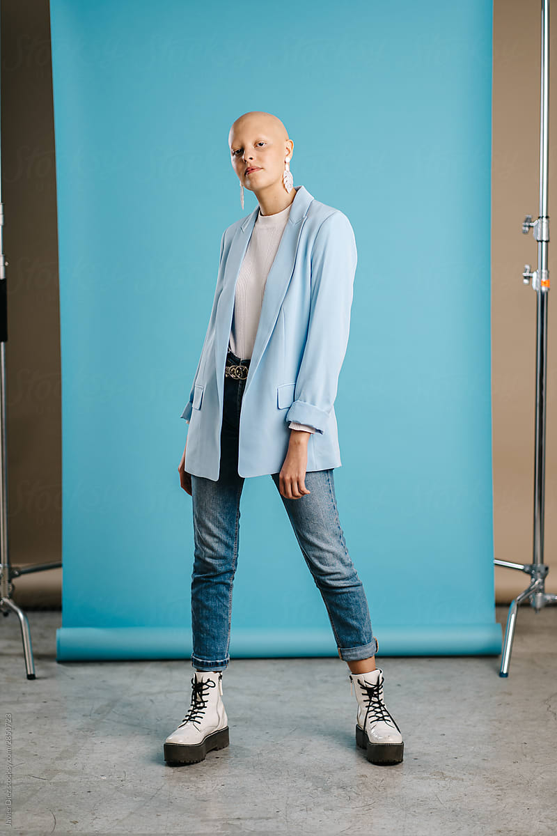 Fashionable bald woman standing against turquoise background