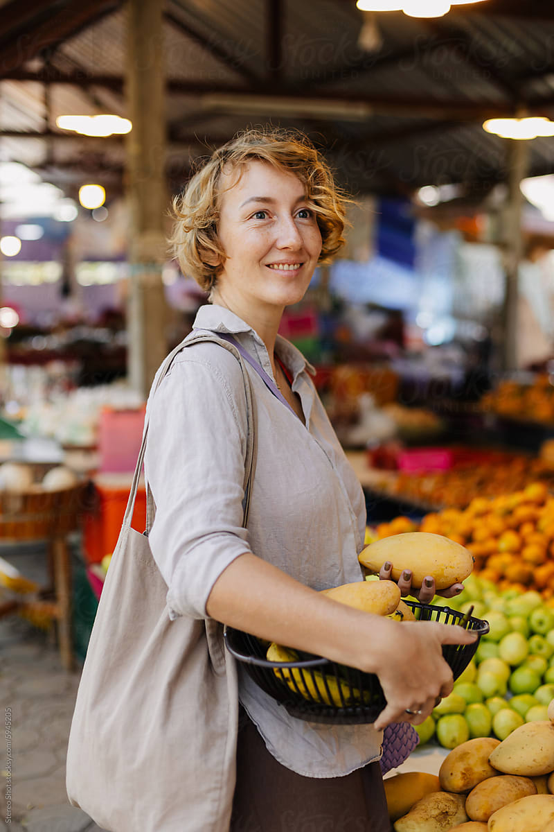 Smiling woman with reusable bag buying fruits at stall