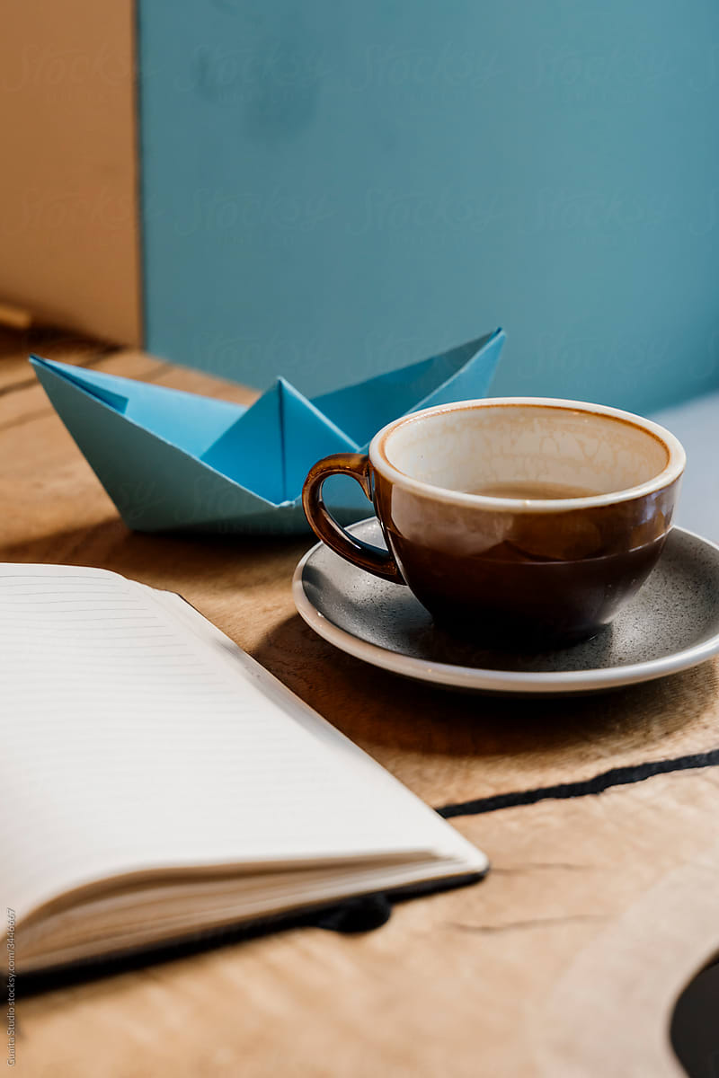 Closeup of notebook coffe mug and origami boat on table