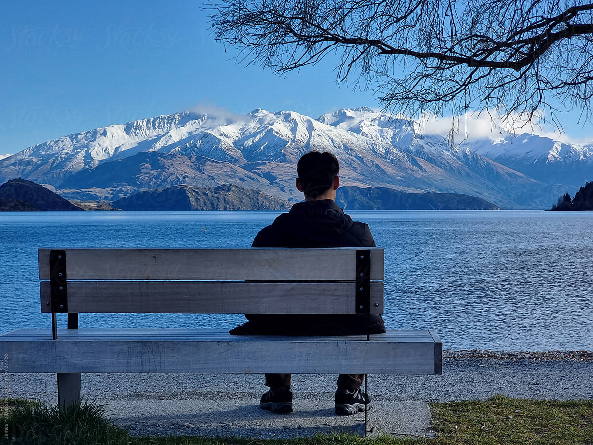 A boy on a bench looking out over the lake and snow capped mountains
