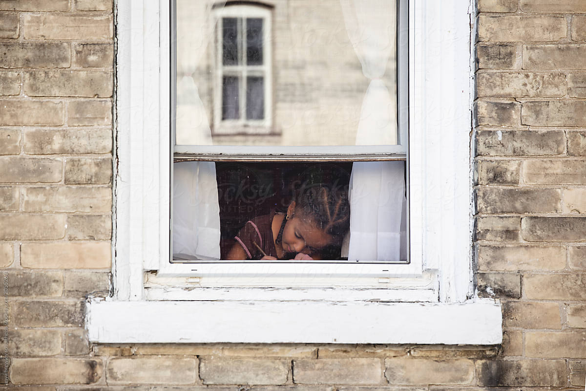 A young child writing in front of a window