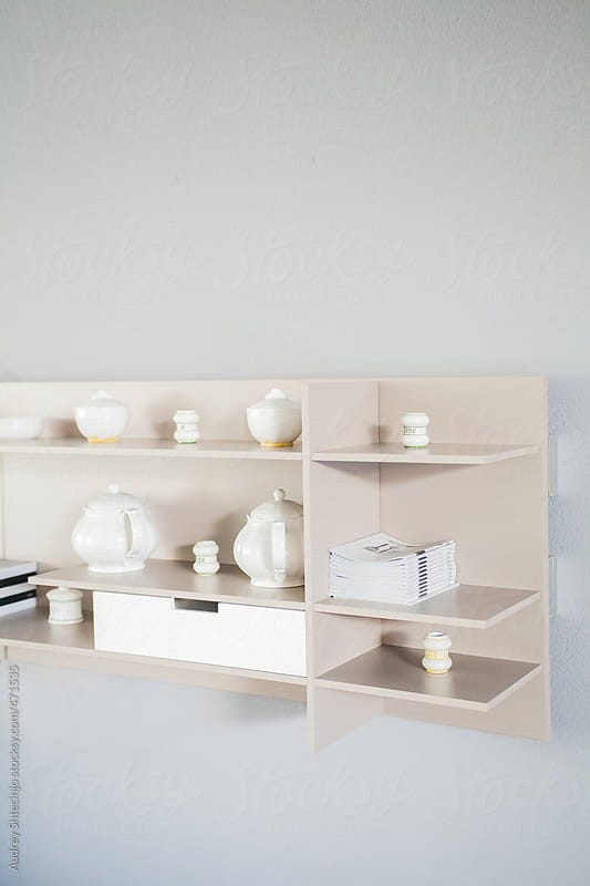 Shelf with white ceramic cups on gray wall.