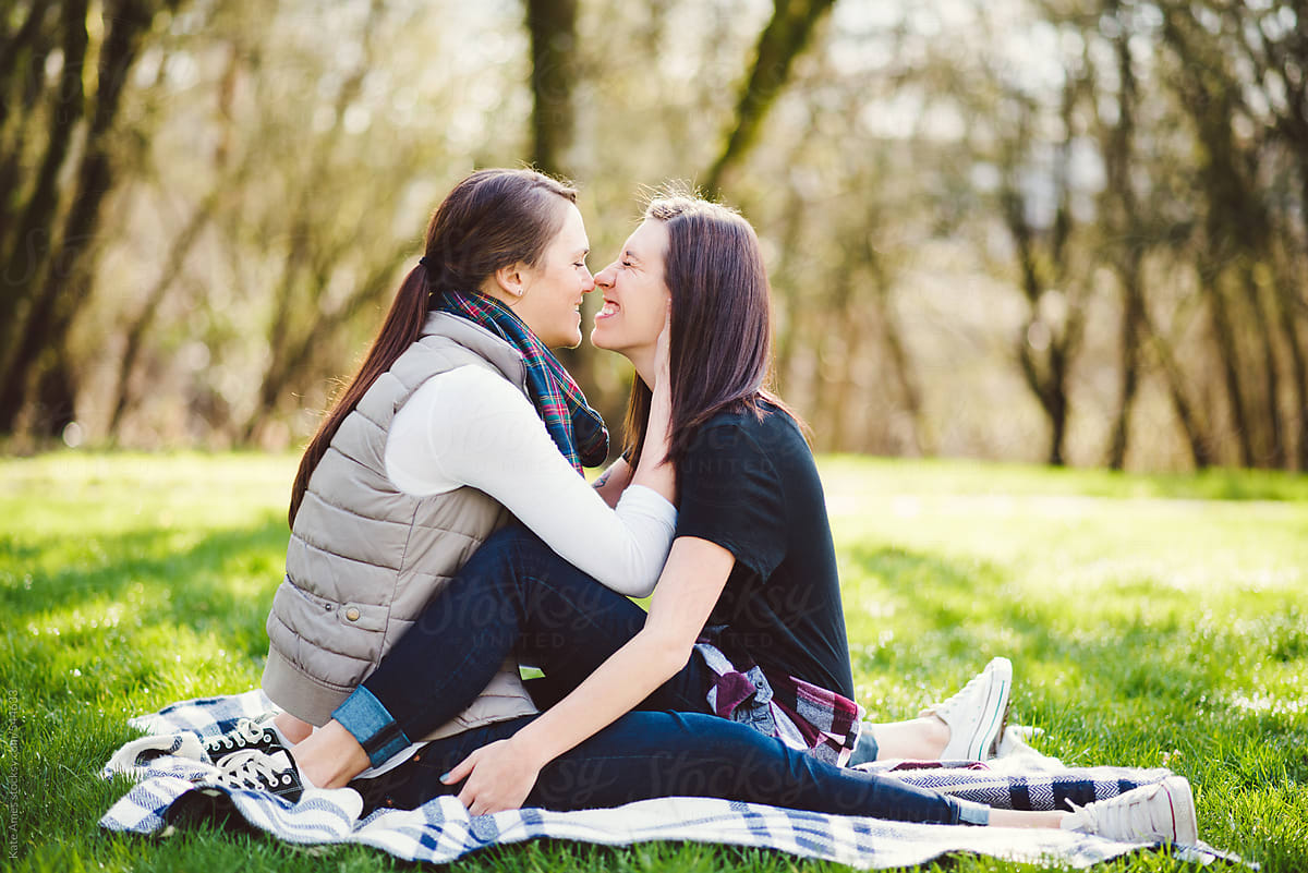 Lesbian couple embracing on a blanket in the park.