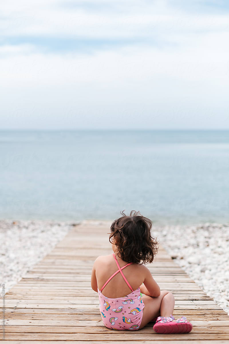 Anonymous girl resting on wooden walkway near seashore
