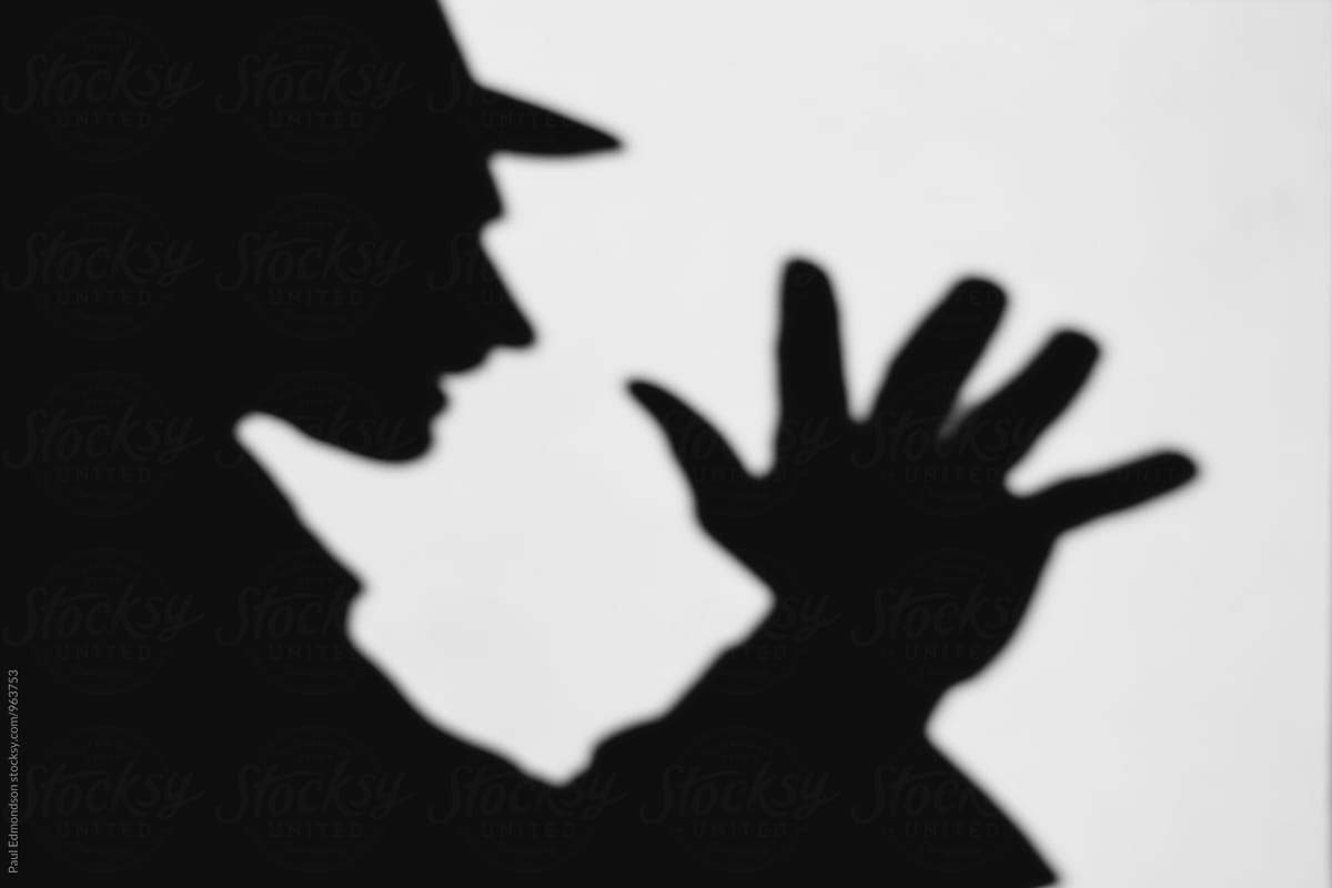 Shadow of man with hand raised, wearing fedora hat