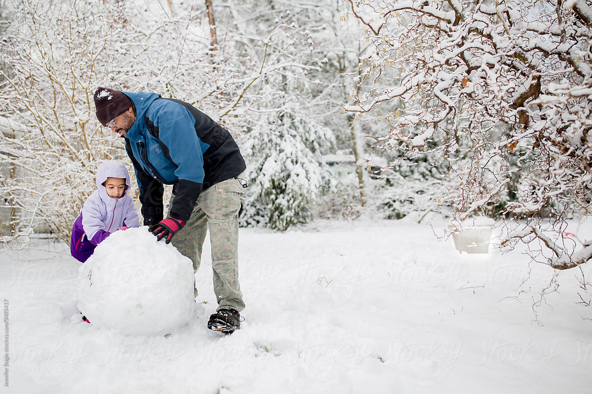 Father and daughter build huge snowball in snowy yard