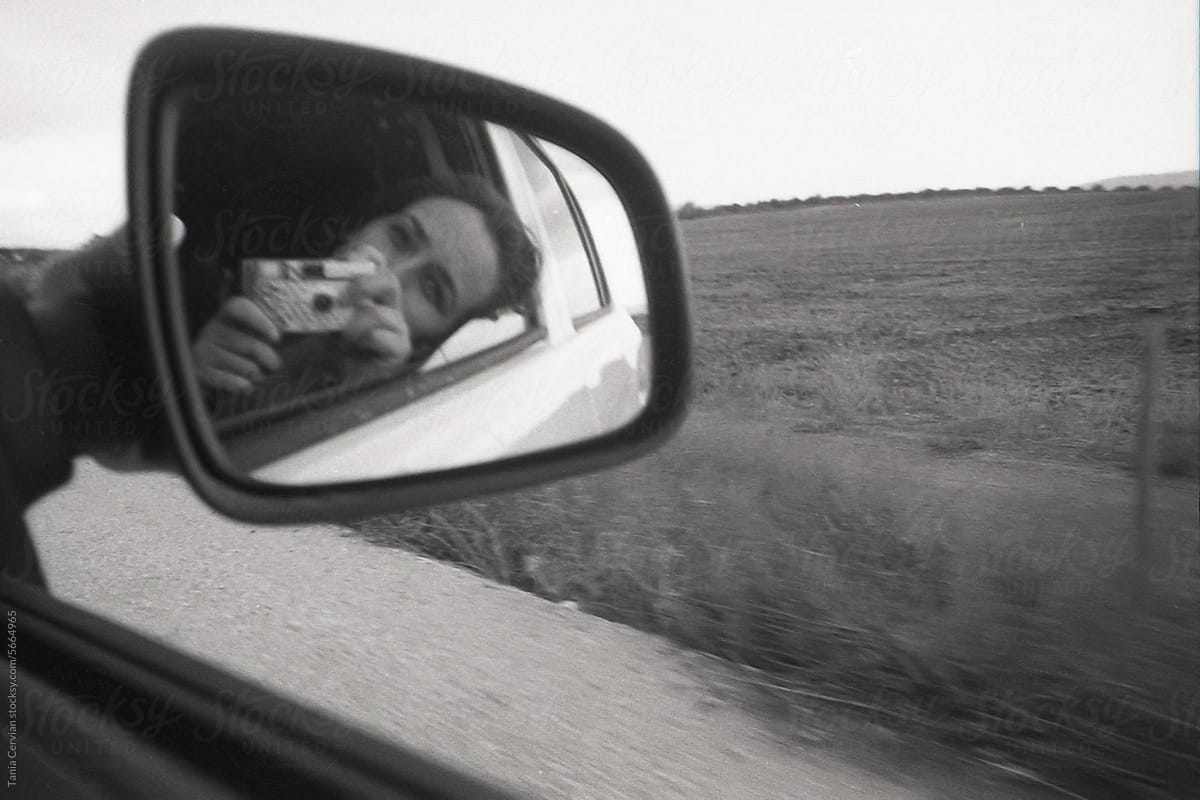 Driving mirror with reflective image of woman taking photo with camera