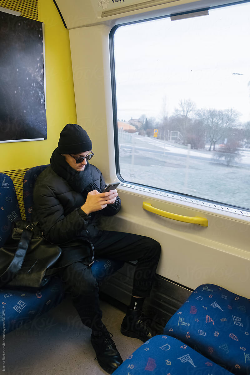 stylish guy in black clothes sits in a subway car and looks at the phone