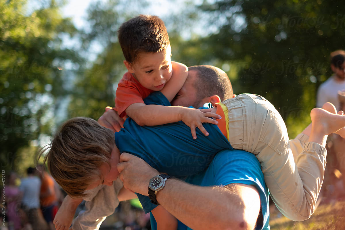 Brothers play, wrestle, climb their father outdoors in a park