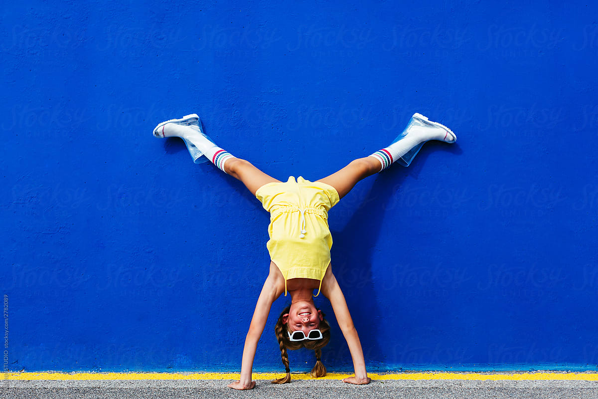 Excited girl with pigtails doing handstand on street