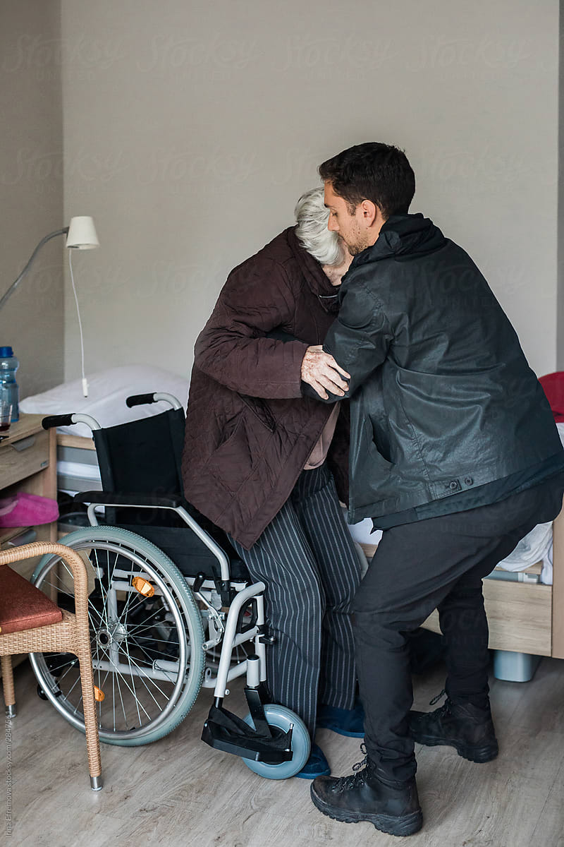 Man helping his grandmother move to a wheelchair from a bed
