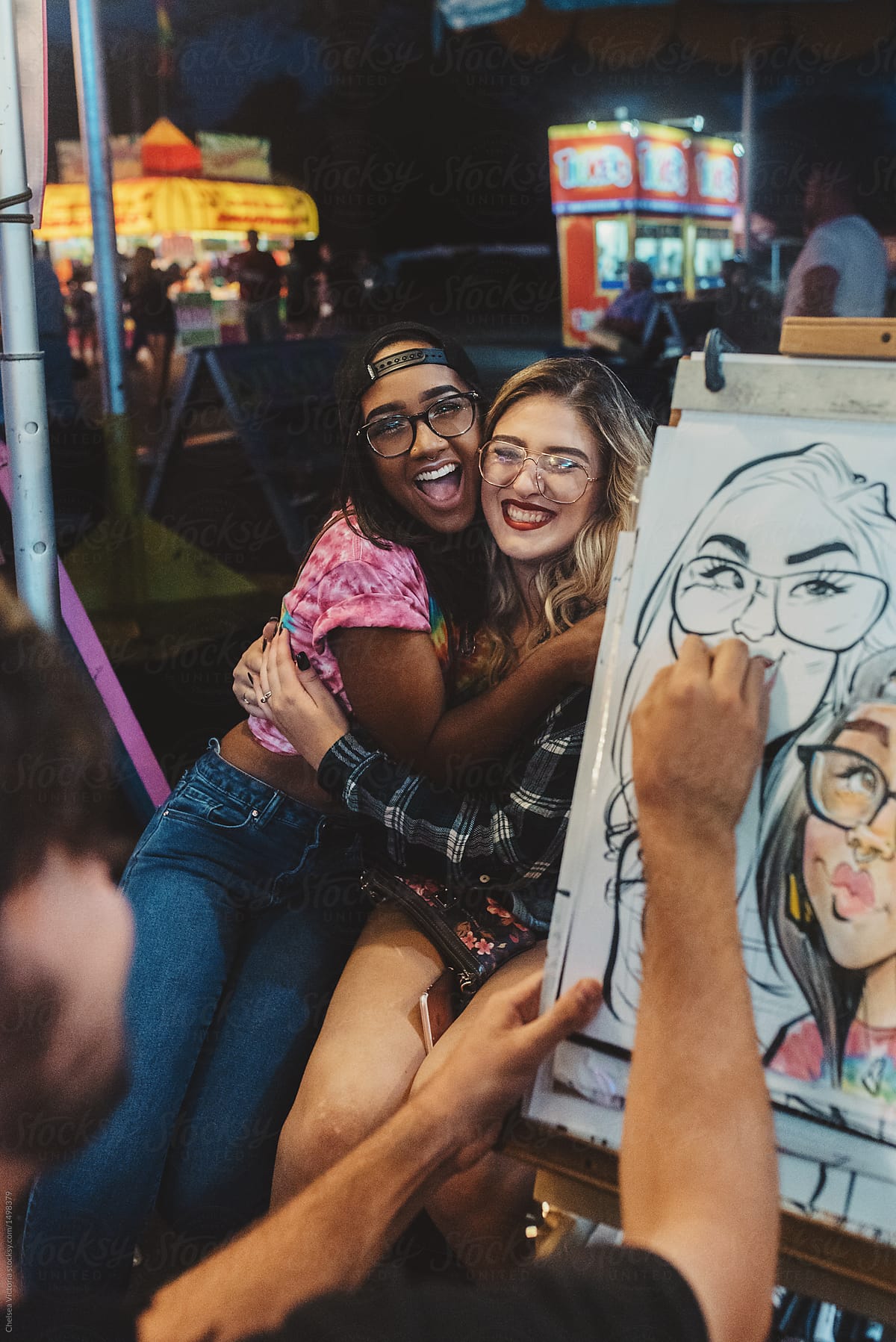 Two Female Friends Having Their Portrait Drawn At A Summer Carnival Del Colaborador De Stocksy 