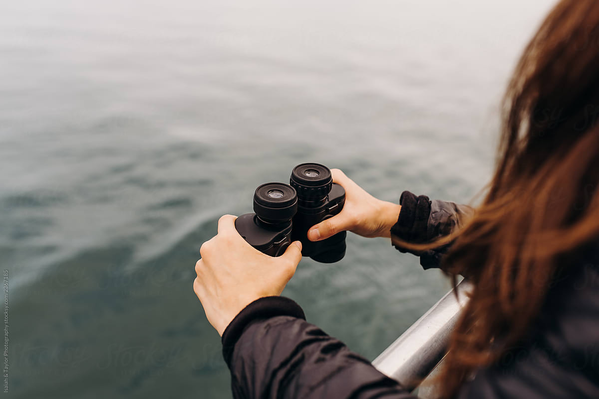 Details of woman\'s hands holding binoculars looking out toward ocean