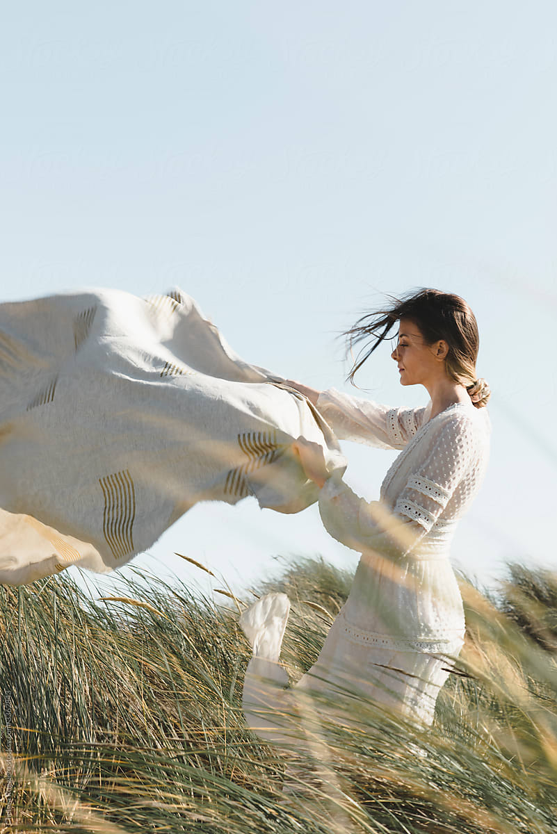 Stylish young woman in grass holding a blanket in the wind