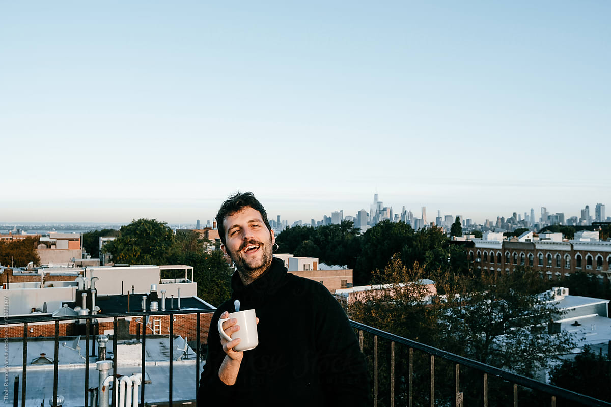 Attractive young man taking a coffee from a rooftop with the New York skyline from behind