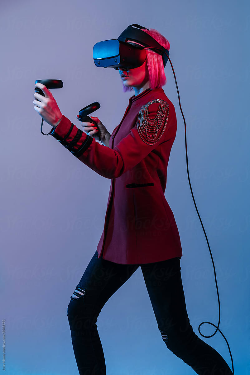 A girl with pink hair in a red jacket and VR Headset in the color light plays with controllers in soe video game