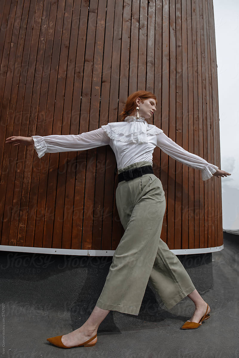 red-haired woman with a dance pose on a background of a wooden wall