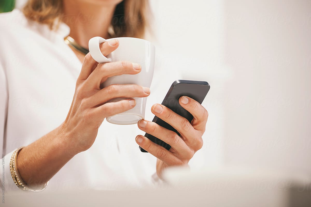 Close up of business woman sending a message with smartphone. Coffee time.