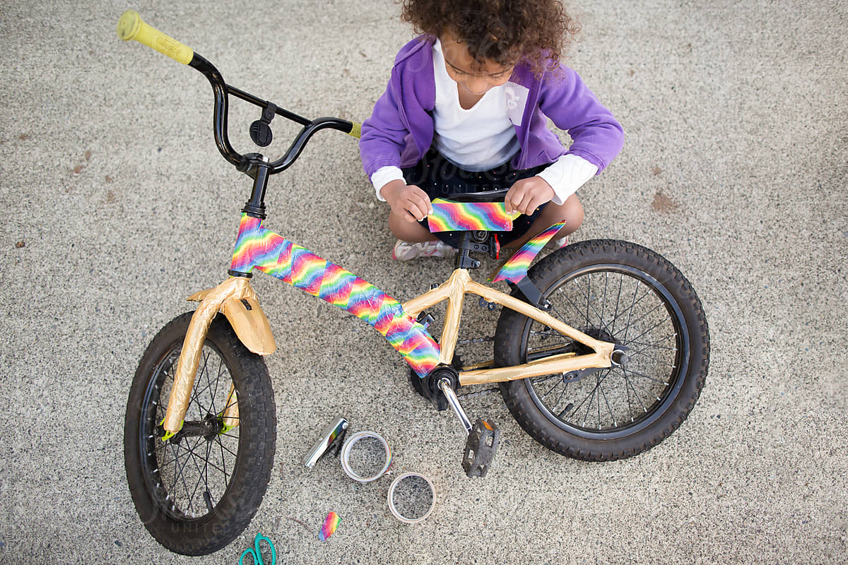Child adds rainbow tape to bicycle