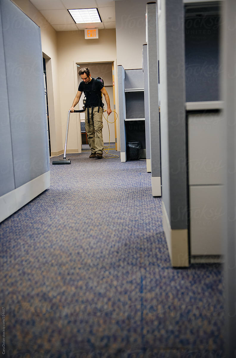 After hours janitor vacuums office carpets