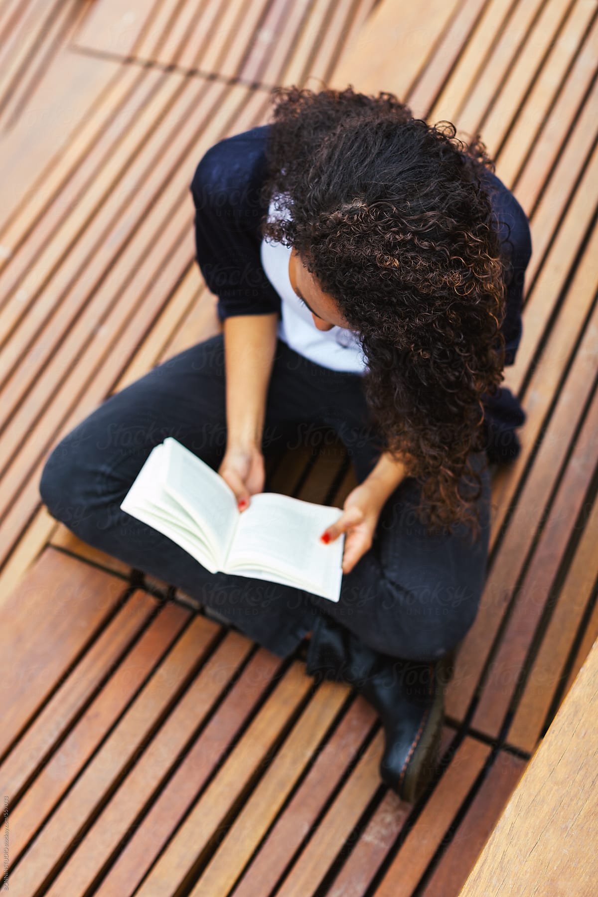 Young african american female reading a book on a wooden floor in outdoors.