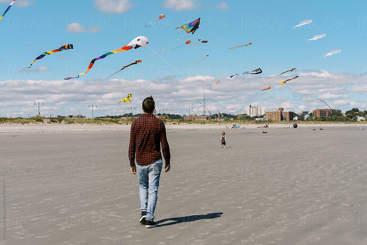 father walking after his toddler who is chasing kites on beach